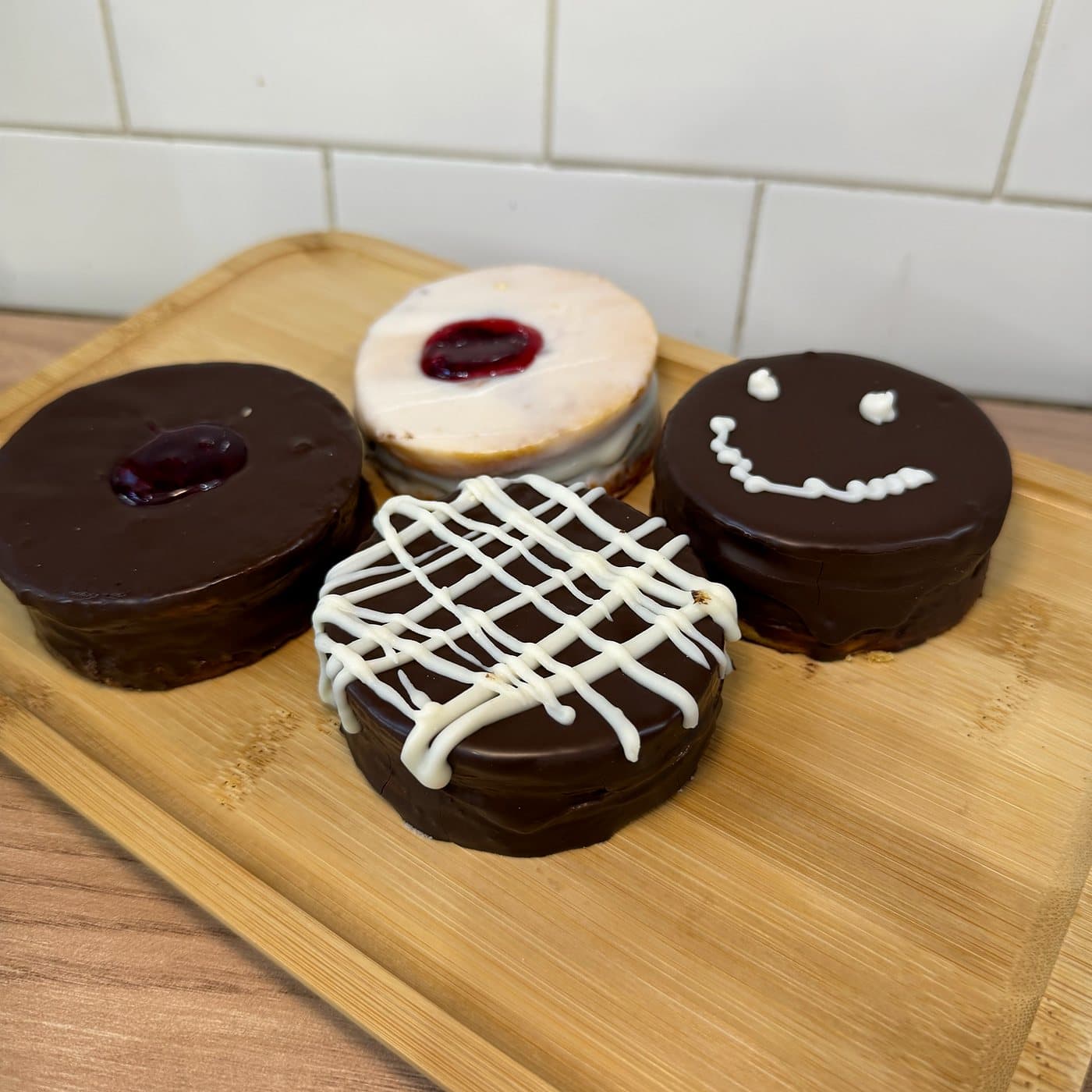 Alfajores bañados en chocolate, decorados con chocolate blanco, mermelada y una carita sonriente