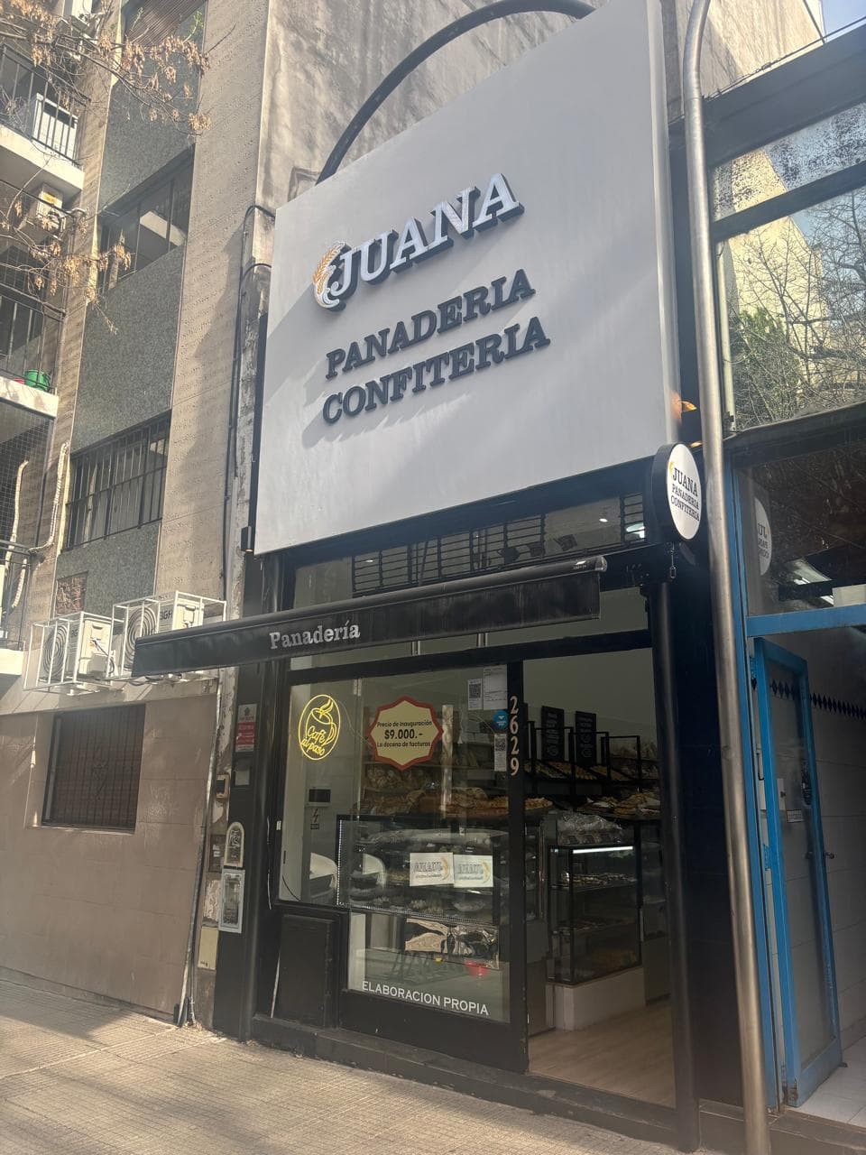 Frente de Panadería Juana en La Pampa 2629: cartel blanco con la palabra Juana, toldo negro y vidriera con el cartel de elaboración propia