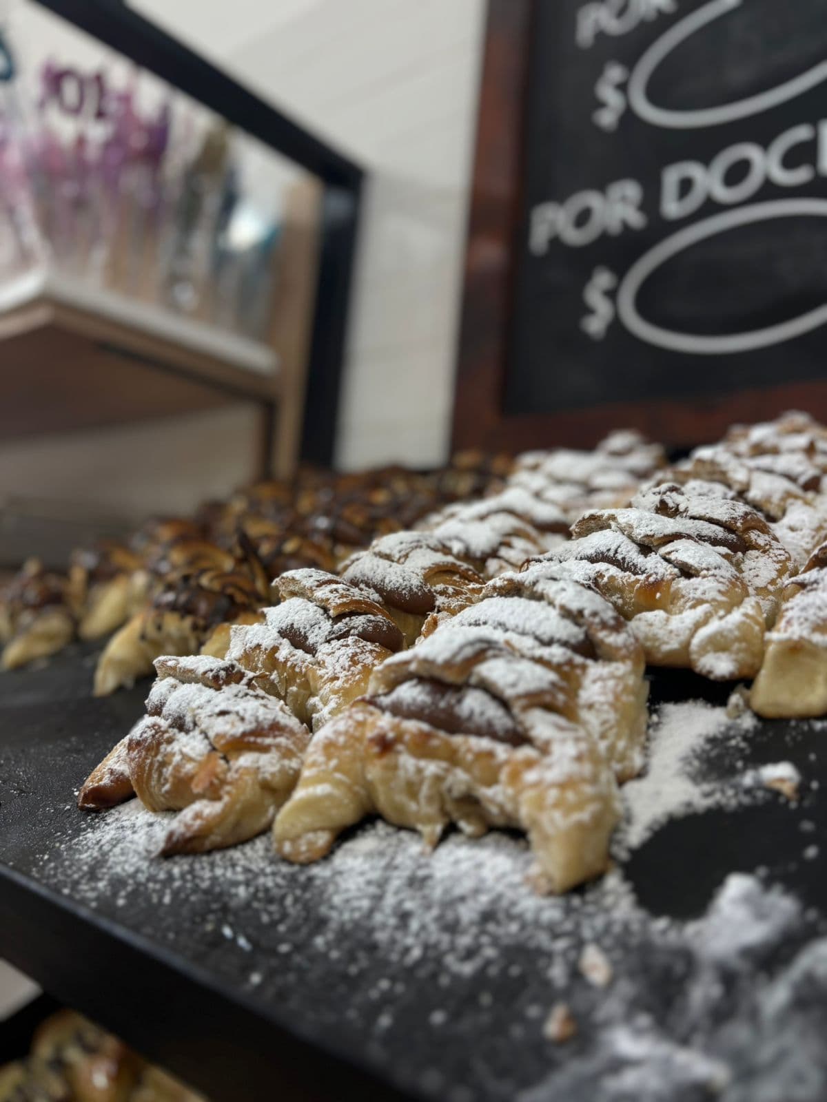 Facturas de hojaldre rellenas, espolvoreadas con azúcar impalpable, sobre una bandeja negra en Panadería Juana