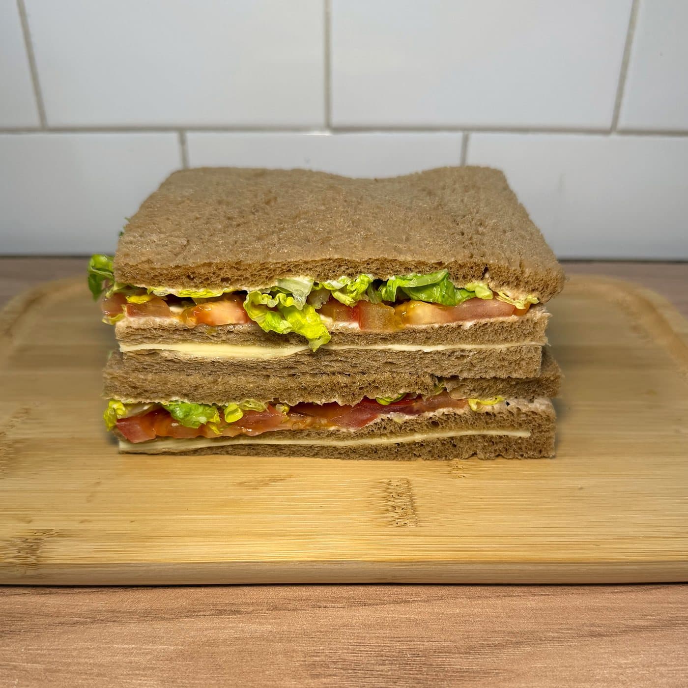 Sándwiches de miga primavera en pan integral, con tomate, lechuga y queso, apilados sobre una tabla