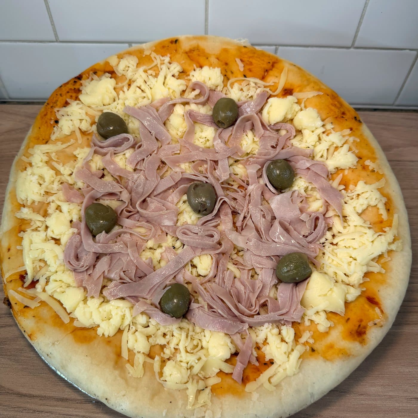 Pizza prelista de muzzarella y jamón con aceitunas verdes