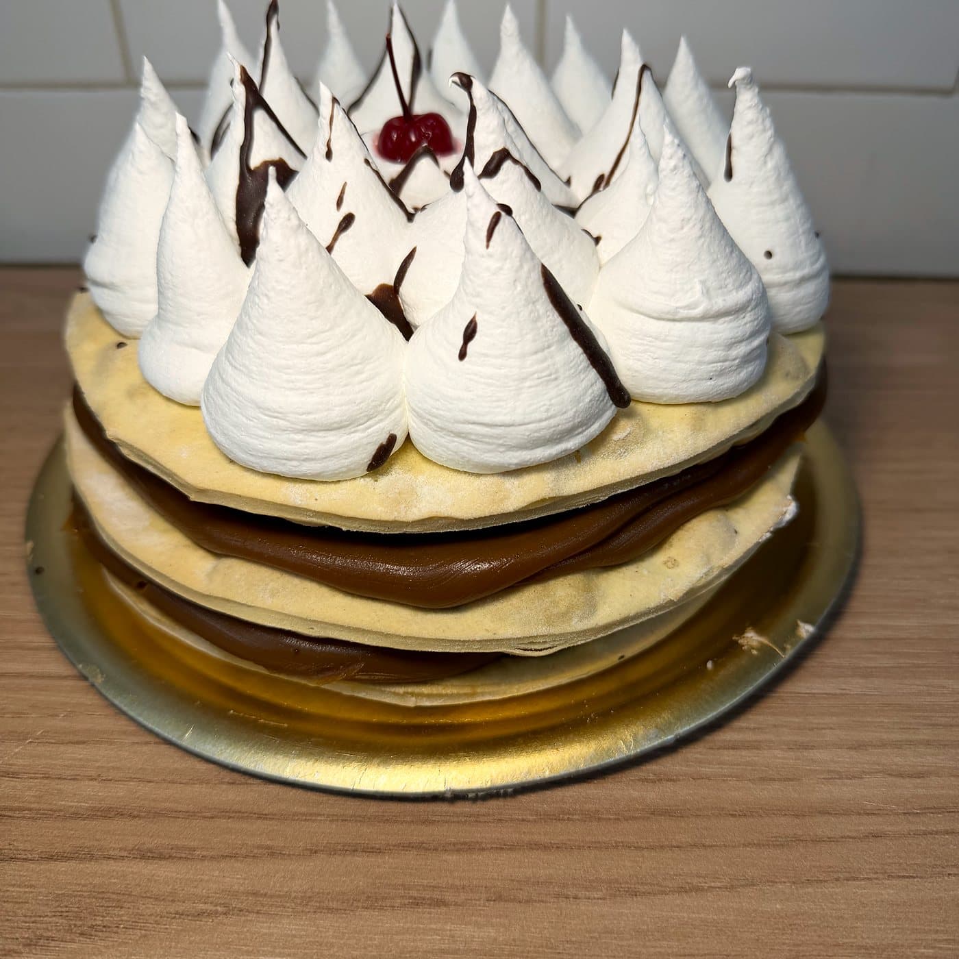 Rogel de capas finas con dulce de leche, cubierto de merengue en picos con hilos de chocolate y una cereza